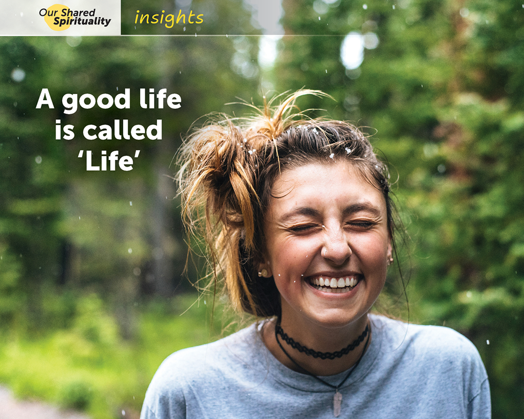 Woman walking outdoors in a forest, grinning as it starts to snow. White text on the image reads A good life is called 'Life'. In a band along the top is a logo for 'Our Shared Spirituality' and the word 'insights'.